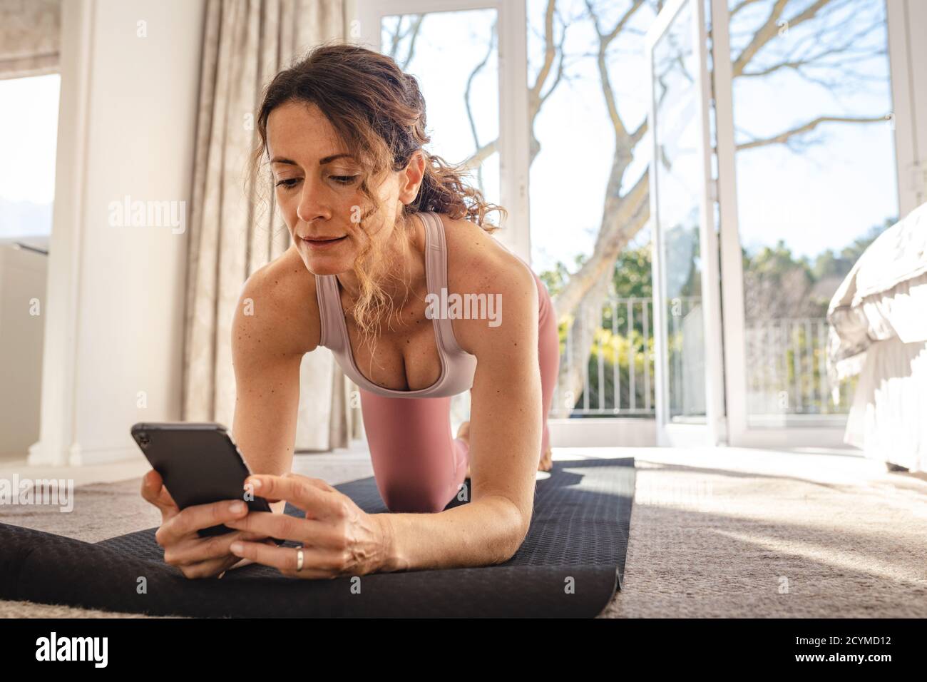 Frau, die Yoga auf der Matte mit Online-Sitzung auf dem Mobiltelefon. Weibliche Arbeit zu Hause in Corona-Virus Pandemie. Stockfoto