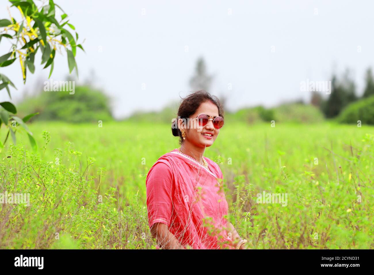 Indische Frau posiert in th Feld in Indian, trägt auf Augen stilvolle Sonnenglas, lachend an der Kamera Stockfoto