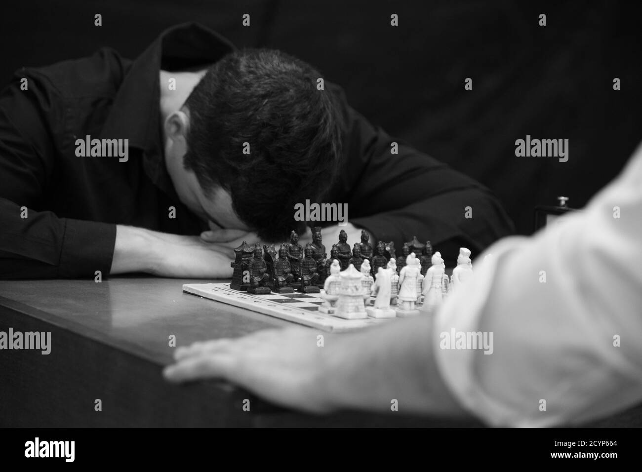 Graustufenaufnahme eines Mannes, der sich in der Niederlage den Kopf verbeugte Nach einem Schachspiel Stockfoto