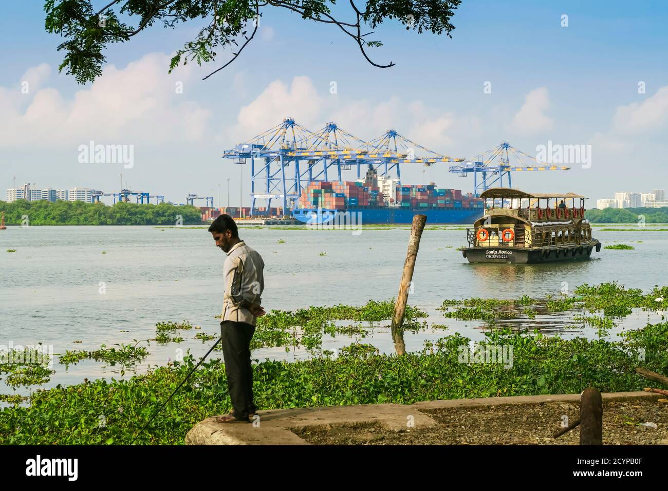 Mann Angeln & Tour Boot in Fort Cochin und Schiff & Krane in Vallarpadam Container Terminal darüber hinaus; Kochi (Cochin), Kerala, Indien Stockfoto