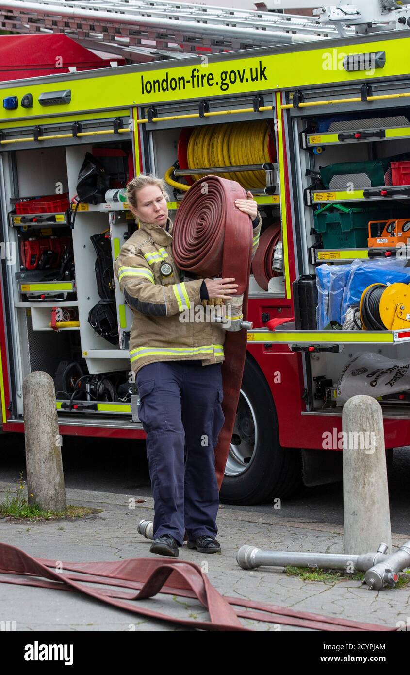 Die Feuerwehrfrau rollt den Schlauch mit der Londoner Feuerwehr aus, die an einem Hausbrand in einer Wohnstraße in South London, England, Großbritannien teilnimmt Stockfoto