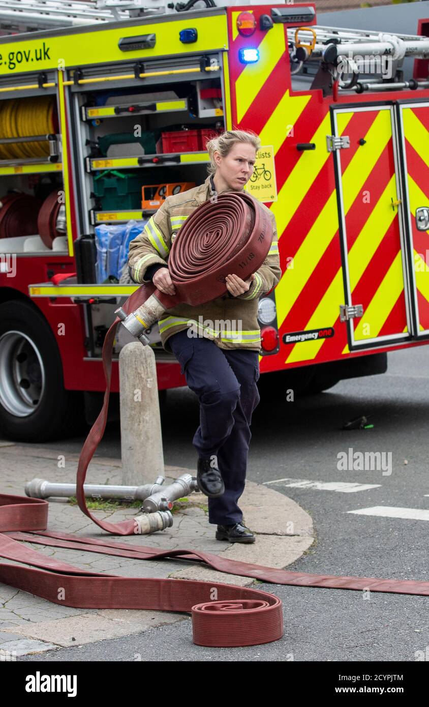 Die Feuerwehrfrau rollt den Schlauch mit der Londoner Feuerwehr aus, die an einem Hausbrand in einer Wohnstraße in South London, England, Großbritannien teilnimmt Stockfoto