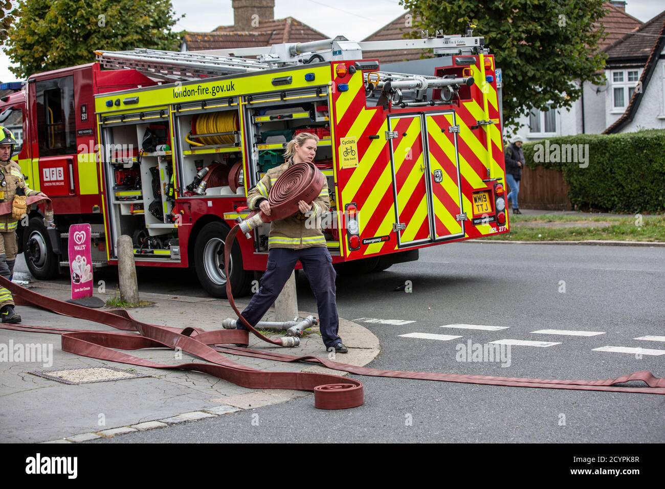 Die Feuerwehrfrau rollt den Schlauch mit der Londoner Feuerwehr aus, die an einem Hausbrand in einer Wohnstraße in South London, England, Großbritannien teilnimmt Stockfoto