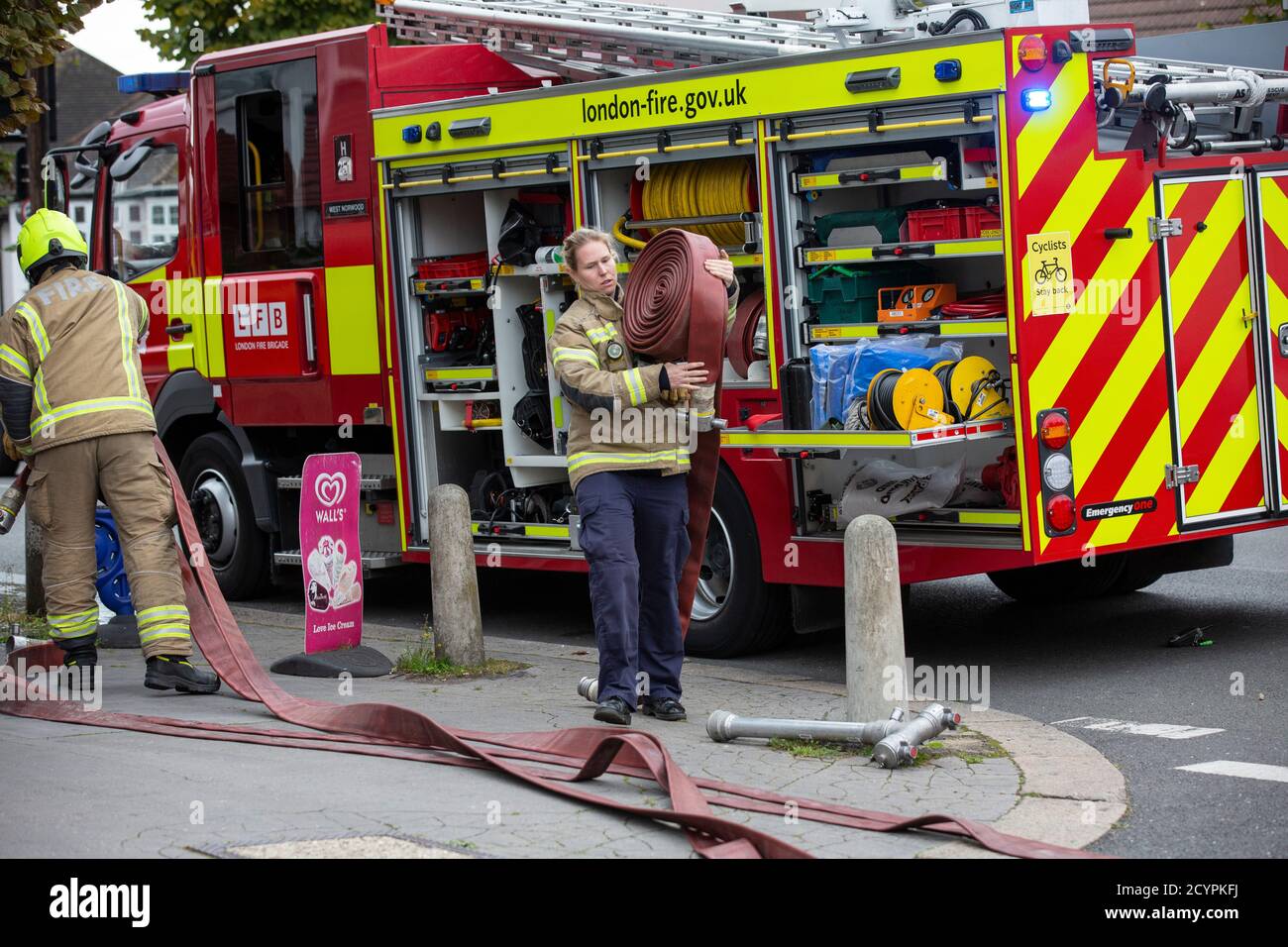 Die Feuerwehrfrau rollt den Schlauch mit der Londoner Feuerwehr aus, die an einem Hausbrand in einer Wohnstraße in South London, England, Großbritannien teilnimmt Stockfoto