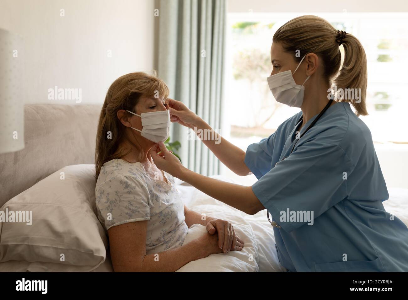 Ältere kaukasische Frau zu Hause von kaukasischen Krankenschwester besucht, setzen eine Gesichtsmaske auf, Krankenschwester trägt Gesichtsmaske. Medizinische Versorgung zu Hause während Covid 1 Stockfoto