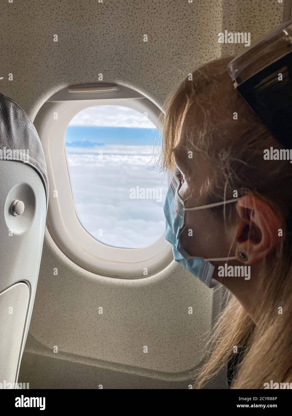 Erwachsene Frau, die mit dem Flugzeug reist und während der Spandemie eine chirurgische Maske trägt. Stockfoto