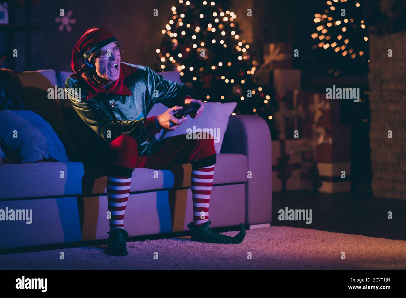 Ganzkörper-Foto von verrückten Elfen sitzen gemütlich Couch spielen Video-Rennspiel im Haus drinnen mit Weihnachten Ornament Nacht Beleuchtung Stockfoto