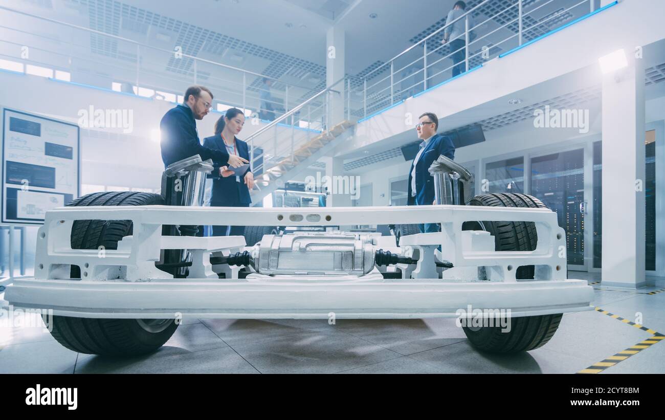 Automobil-Design-Ingenieure sprechen während der Arbeit an Elektro-Auto-Chassis-Prototyp. In Innovation Laboratory Facility Konzept Fahrzeug Rahmen Umfasst Stockfoto