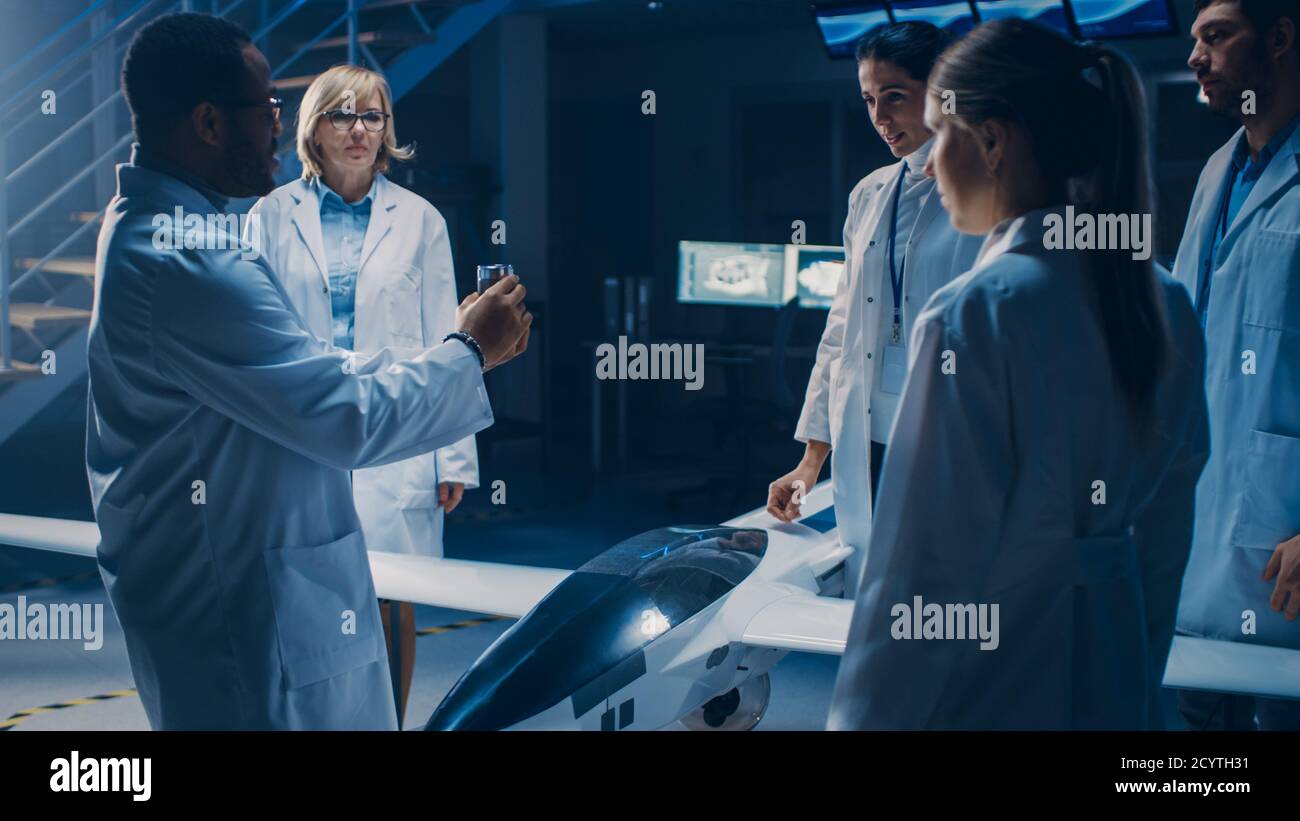 Treffen der Luft- und Raumfahrtingenieure, die am unbemannten Luftfahrzeug-Drohne-Prototyp arbeiten. Luftfahrtwissenschaftler in White Coats sprechen. Gewerbliches Luftbild Stockfoto