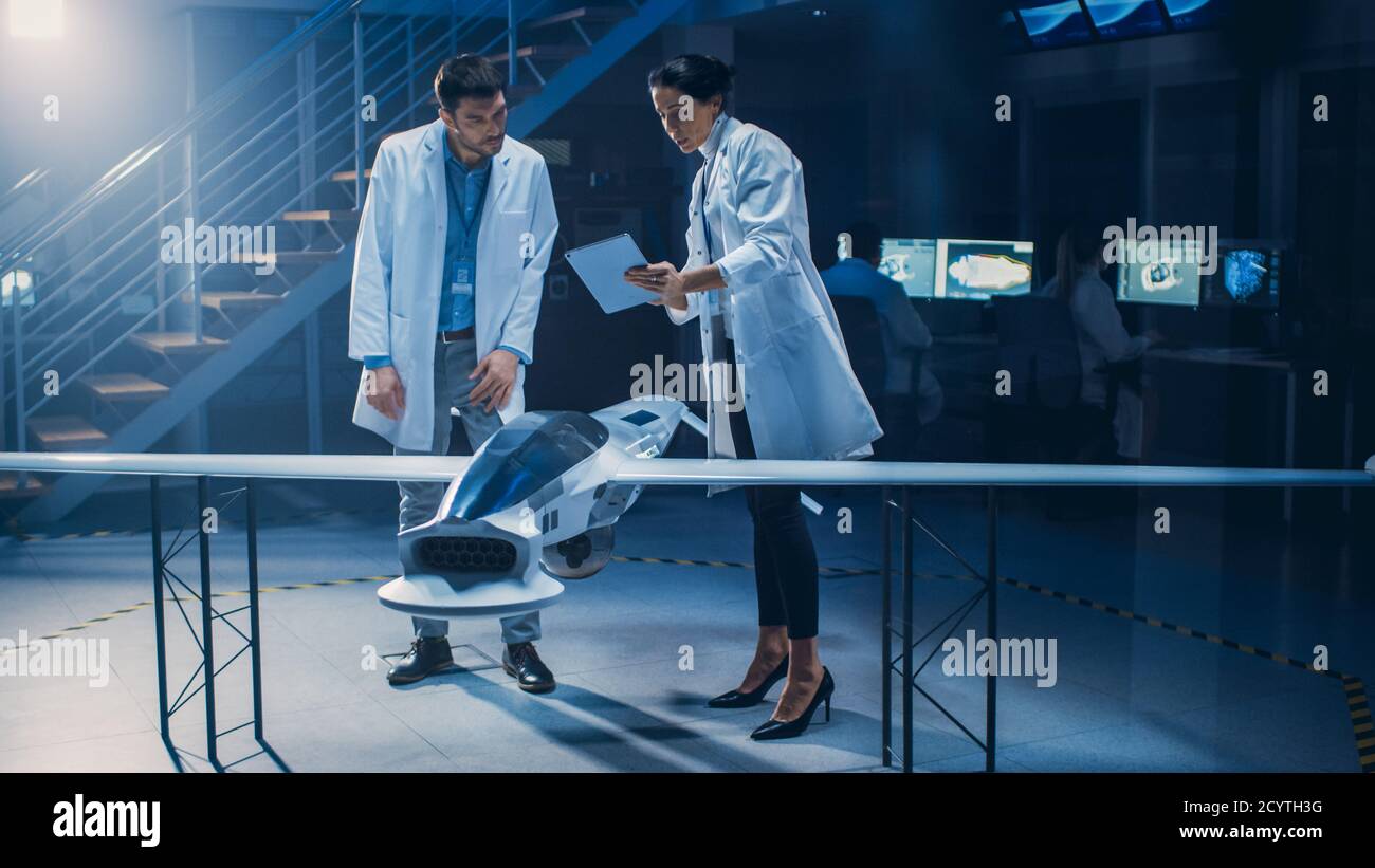 Treffen der Luft- und Raumfahrtingenieure, die am unbemannten Luftfahrzeug-Drohne-Prototyp arbeiten. Luftfahrtwissenschaftler in White Coats sprechen. Gewerbliches Luftbild Stockfoto