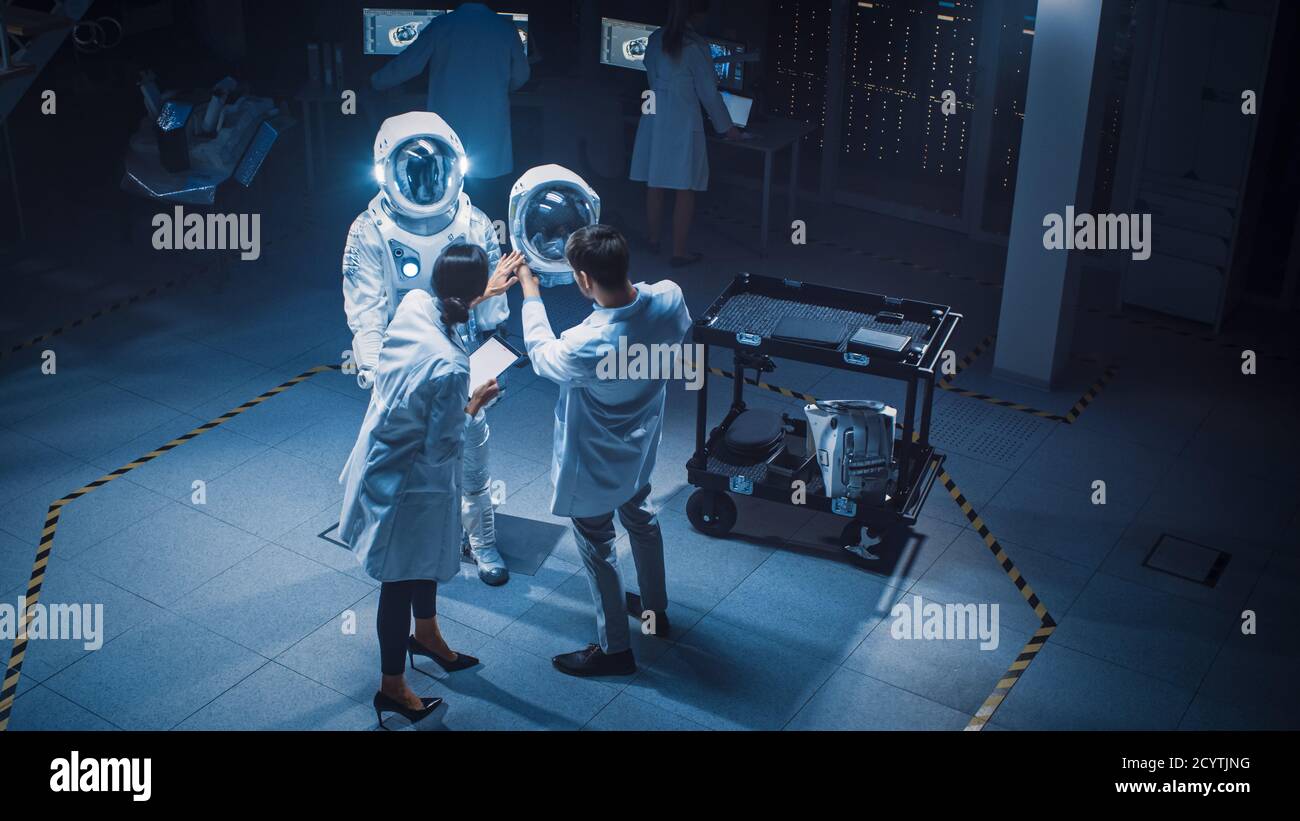 Aerospace Einrichtung: Wissenschaftler, Ingenieure tragen weiße Mäntel haben Diskussion, verwenden Computer, konstruieren Astronaut Helm für neue Raum Anzug angepasst Stockfoto