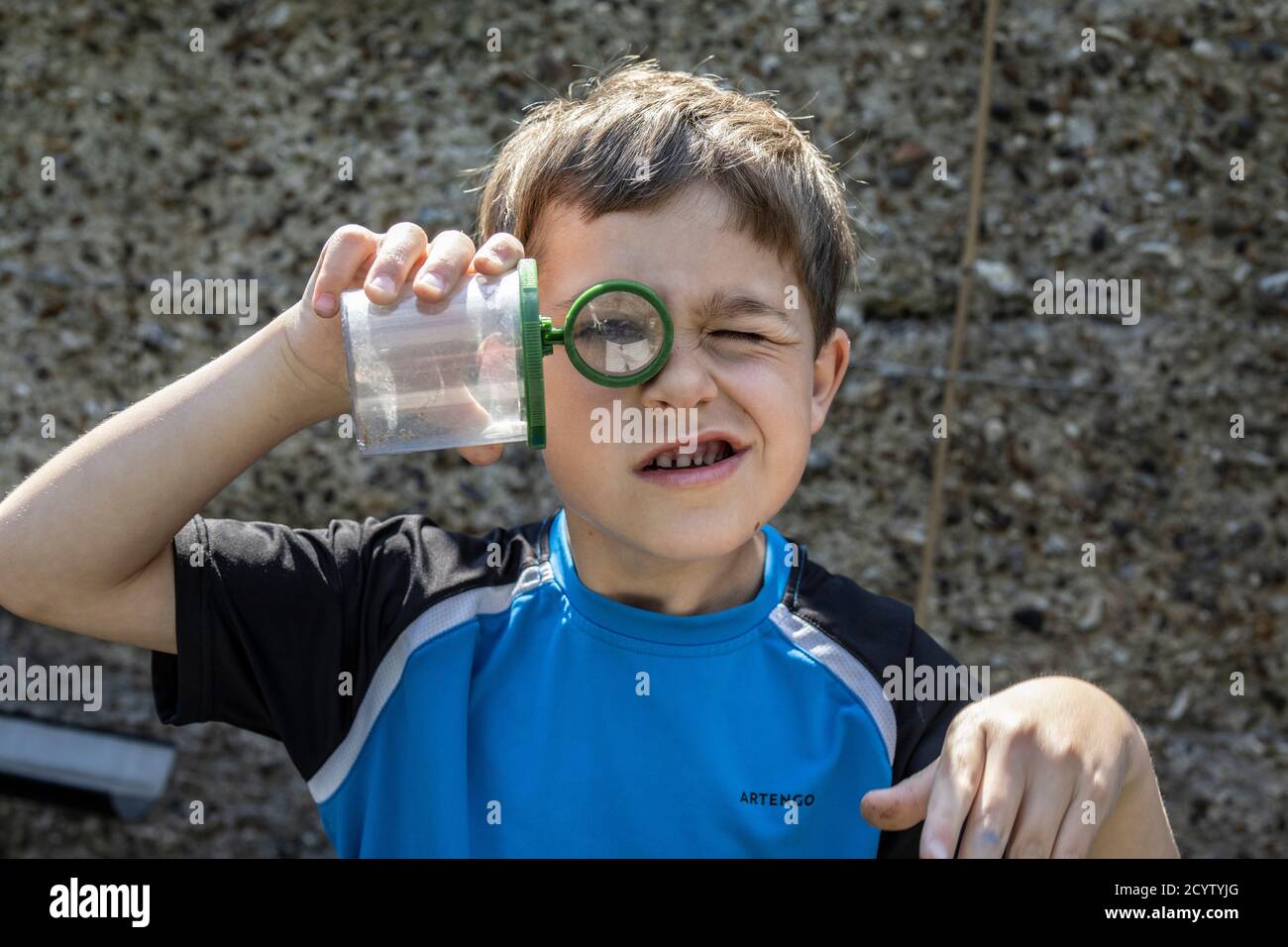 Sechs Jahre alter Junge schaut durch eine Lupe in seinem Garten, während er nach Insekten sucht, England, Großbritannien Stockfoto