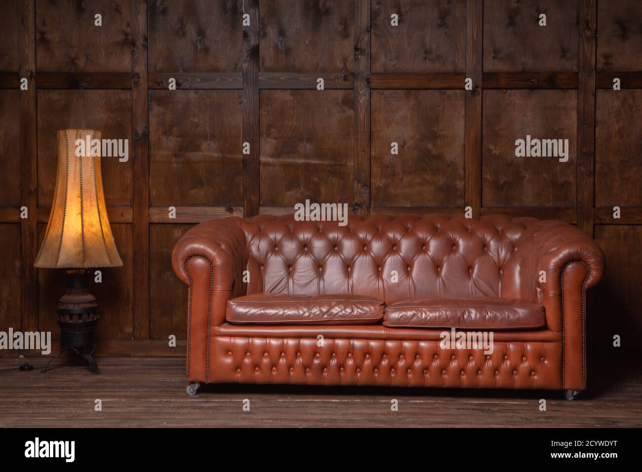 Einrichtung im klassischen braunen Loft-Stil mit Holztäfelung, chesterfield-Sofa. Altes Sofa auf dem Hintergrund der Vintage-Wand. Hochwertige Fotos Stockfoto