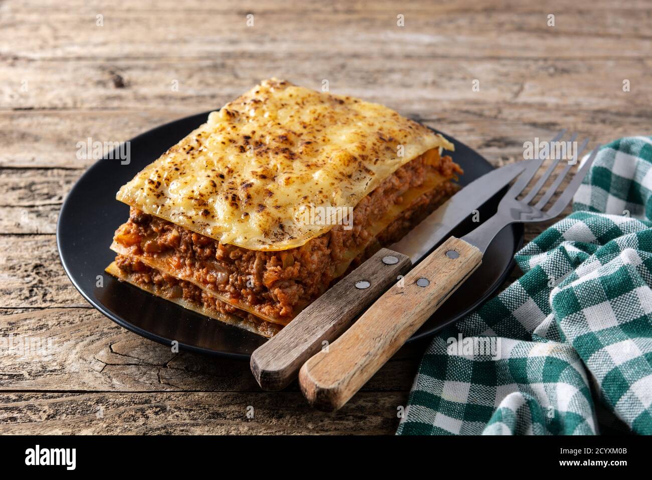 Stück Lasagne auf schwarzem Teller auf rustikalem Holz Tabelle Stockfoto