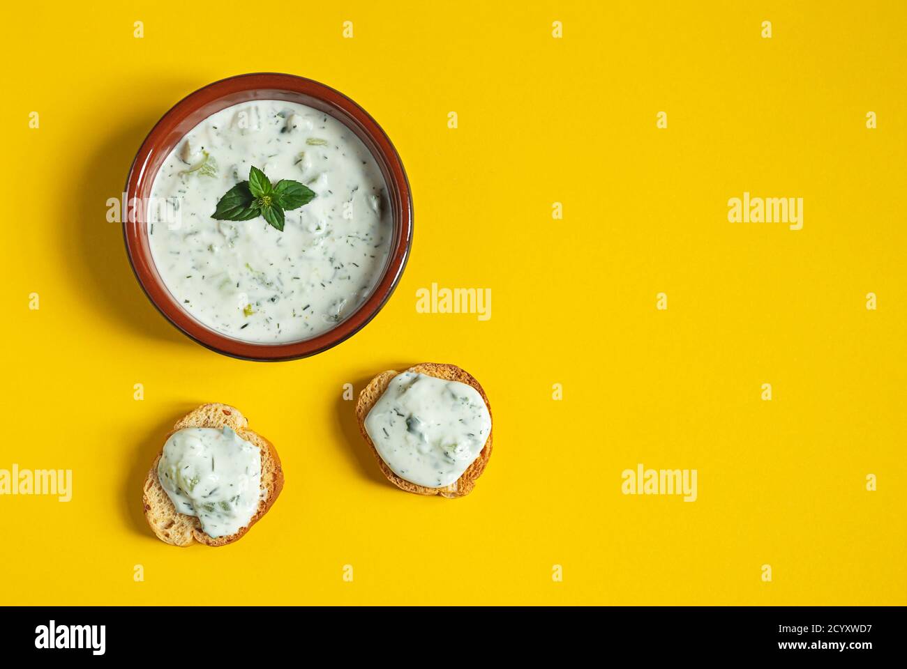 Eine Schüssel und Crostini oder Bruschetta mit traditionellen griechischen Tzatziki Sauce isoliert auf dem gelben Hintergrund Stockfoto