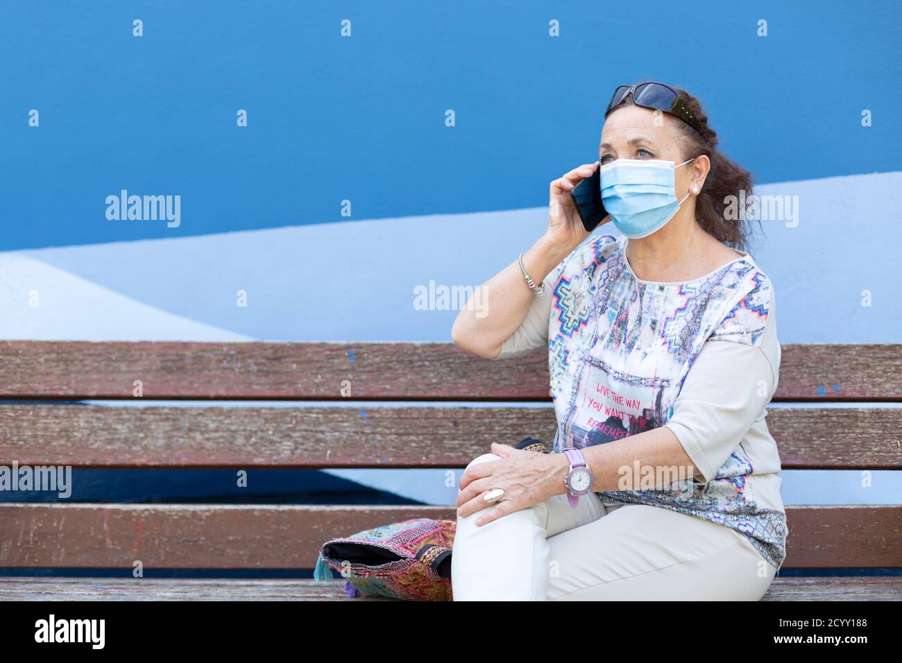 Reife Frau mit einer medizinischen Maske sprechen am Telefon. Sie ist draußen. Leerzeichen für Text. Stockfoto