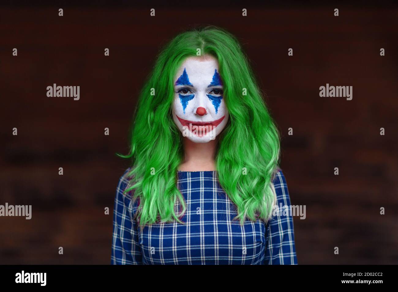 Nahaufnahme Porträt eines grünhaarigen Mädchen in gechicktem Kleid mit Joker Make-up auf einem verschwommenen braunen Hintergrund. Stockfoto