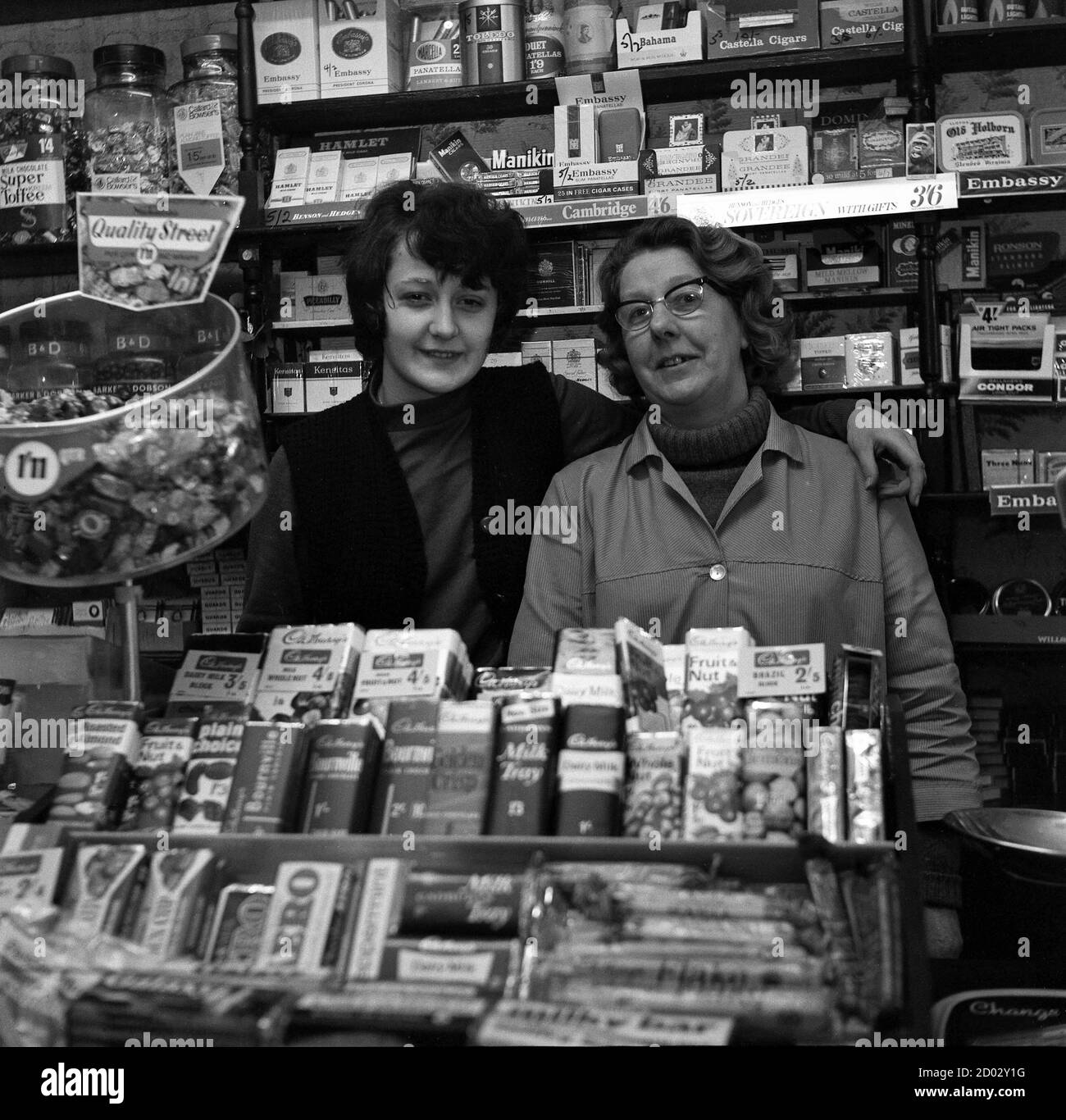 AJAXNETPHOTO. 1970. SOUTHSEA, ENGLAND. - SÜSSIGKEITEN UND TABAK - FRAU CROSS (RECHTS) INHABERIN DES CARLTON TABAKWARENHANDELS UND SÜSSWARENLADEN IN KENT ROAD MIT IHREM SOHN.FOTO:JONATHAN EASTLAND/AJAX REF:1970 21 Stockfoto