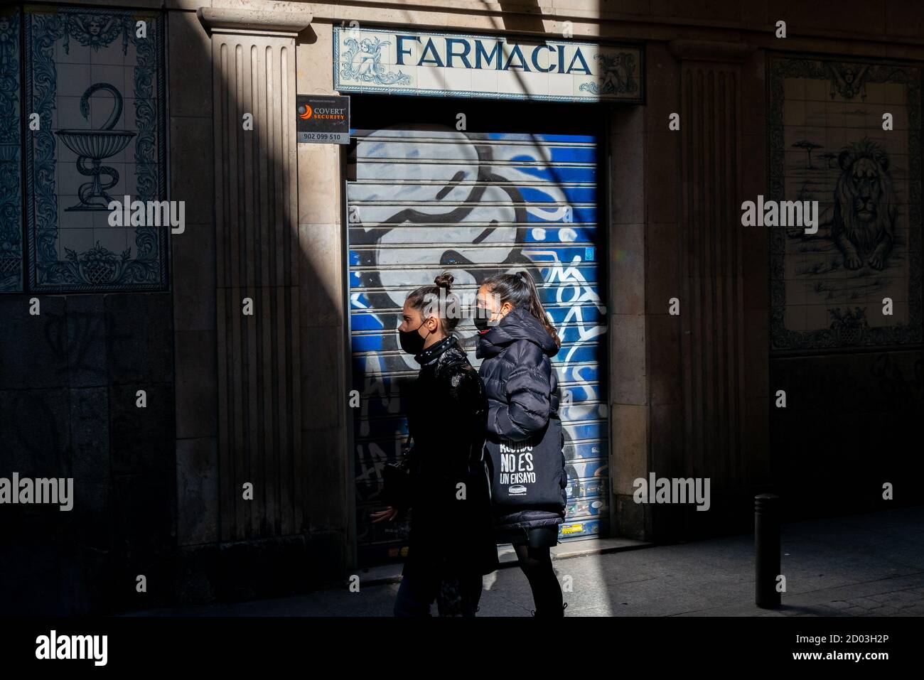 Frauen mit Gesichtsmasken gehen an einer geschlossenen Apotheke vorbei.heute sind in Madrid die von der Regierung geforderten Haftmaßnahmen zur Bekämpfung der Pandemie in Kraft getreten. Beschränkung des ein- und Ausgangs in Wohngebieten, Reduzierung der sozialen und familiären Versammlungen auf maximal sechs Personen, Restaurants schließen um 10 Uhr und haben eine maximale Kapazität von 50%. Stockfoto