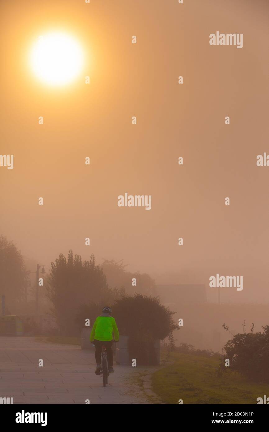 Mann in einer gelben Weste, der sein Fahrrad auf einem fährt Nebliger Morgen in Steveston British Columbia Kanada Stockfoto