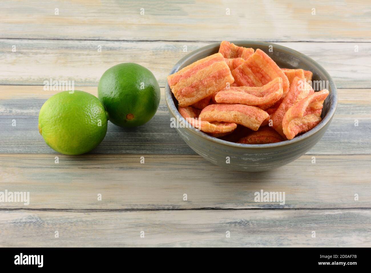 Geblasen Speck Chips gewürzt mit Zingy Linie in Keramik-Schüssel Mit zwei frischen Limetten auf dem Tisch Stockfoto
