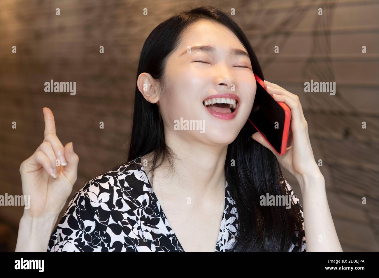 Sehr glückliche chinesisch-amerikanische Frau mit einem roten Smartphone In einem Café mit Kopierplatz Stockfoto