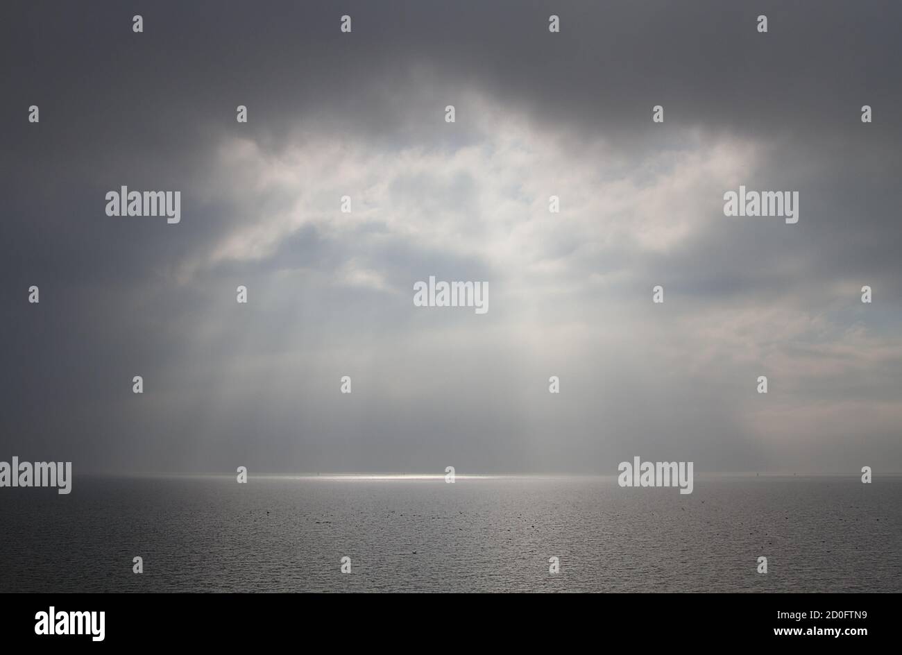 Die Sonne bricht durch die Wolken über einem nebligen, ruhigen Meer Stockfoto