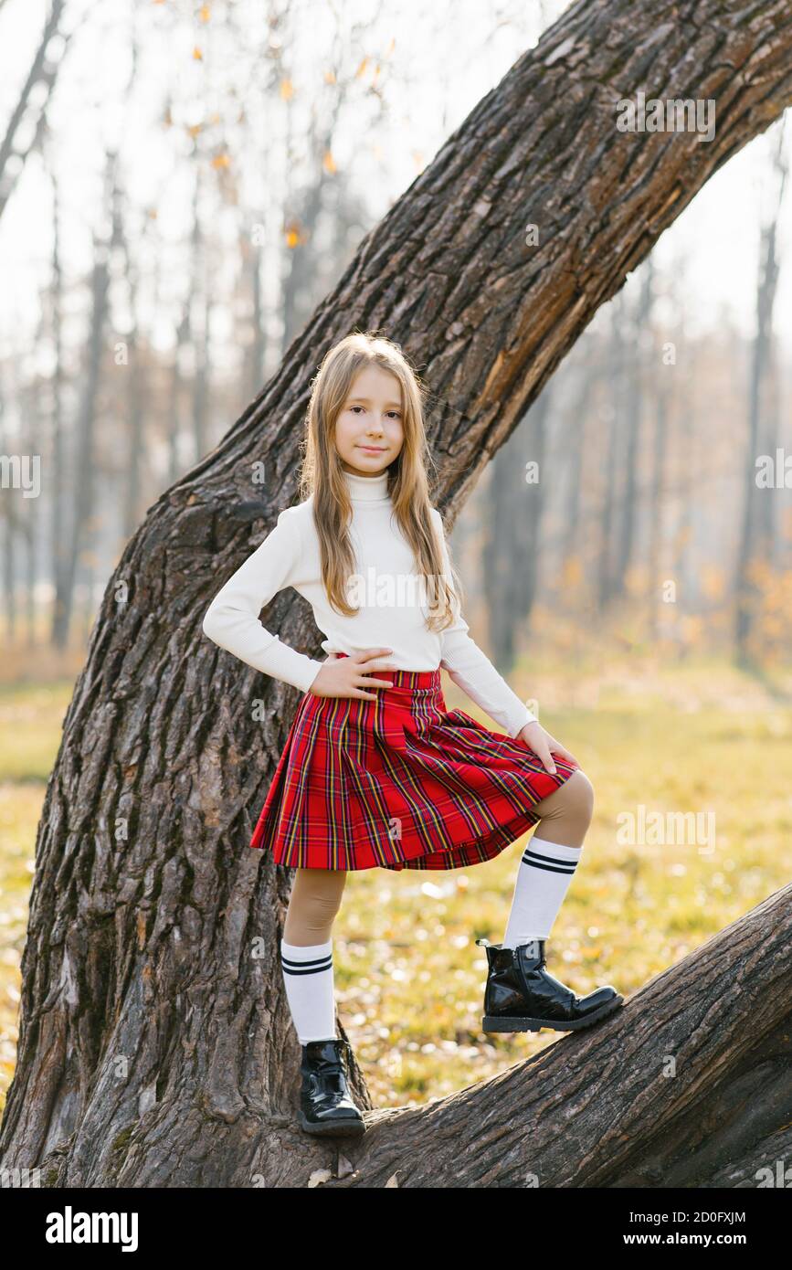 Ein Teenager-Mädchen in einem roten Rock und weißen Pullover Steht auf einem Baum in einem Herbstpark und lächelt Stockfoto