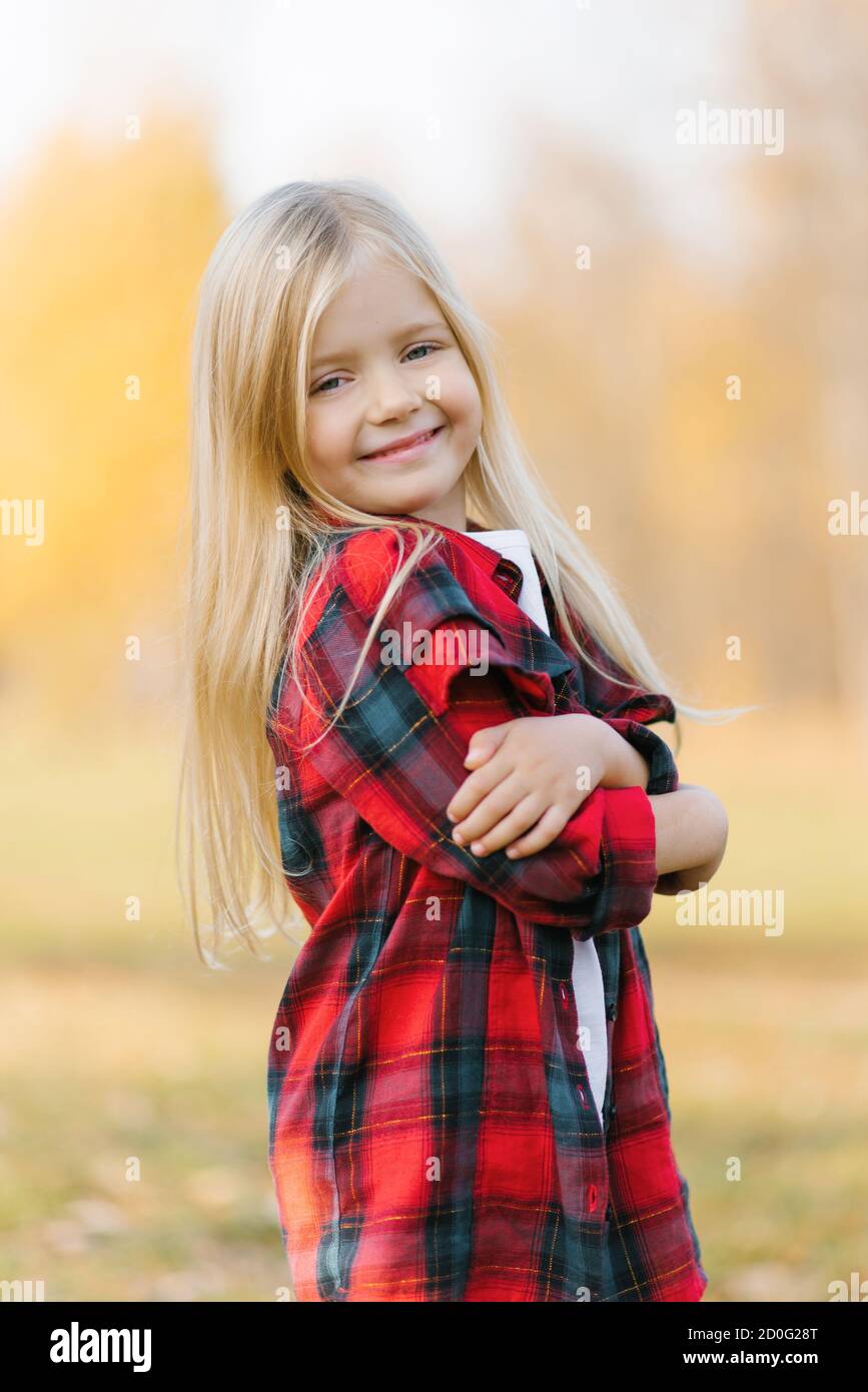 Porträt eines lächelnden kleinen Mädchens in einem rot karierten hemd mit blonden Haaren in einem Herbstpark Stockfoto