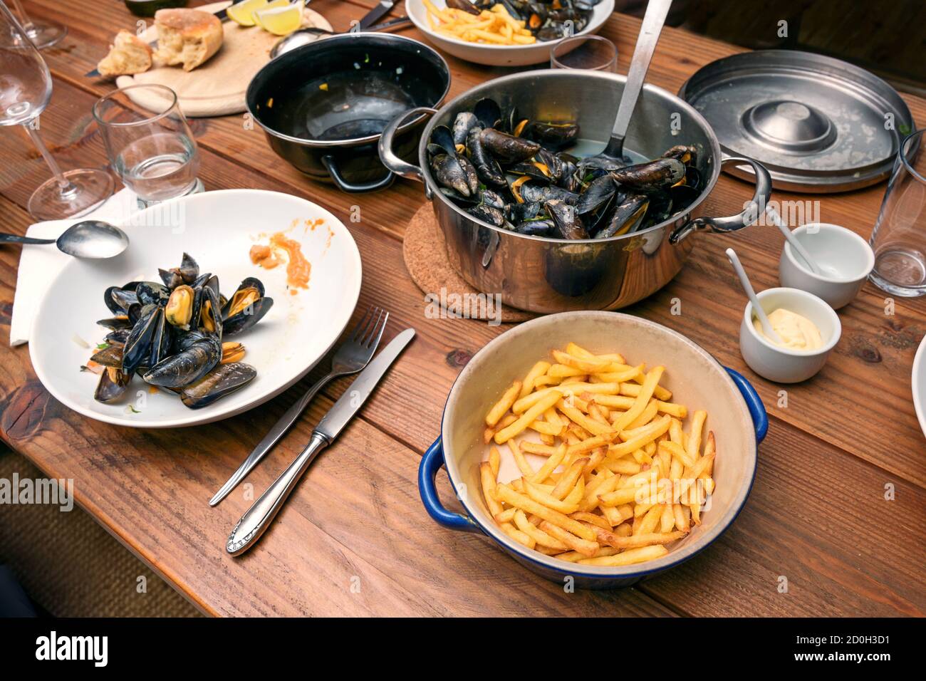 Blaue Muscheln im Topf und Pommes Frites, Teller, Gläser und Besteck auf einem rustikalen Holztisch, traditionelle informelle Mahlzeit mit Familie oder Freunden, wählen Stockfoto