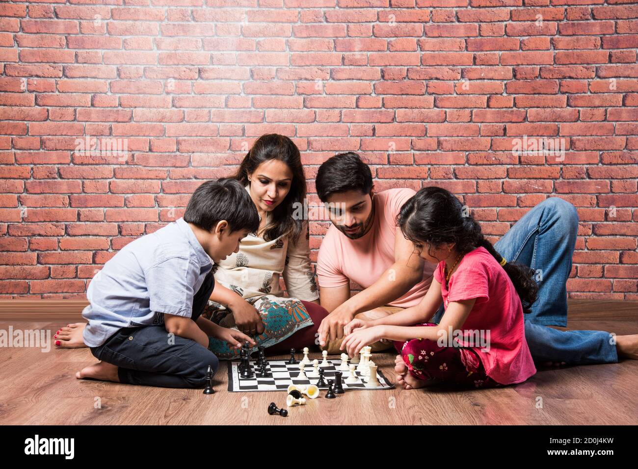 Indische junge Familie von vier spielen Brettspiele wie Schach, Ludo oder Snack und Leiter zu Hause in Quarantäne Stockfoto