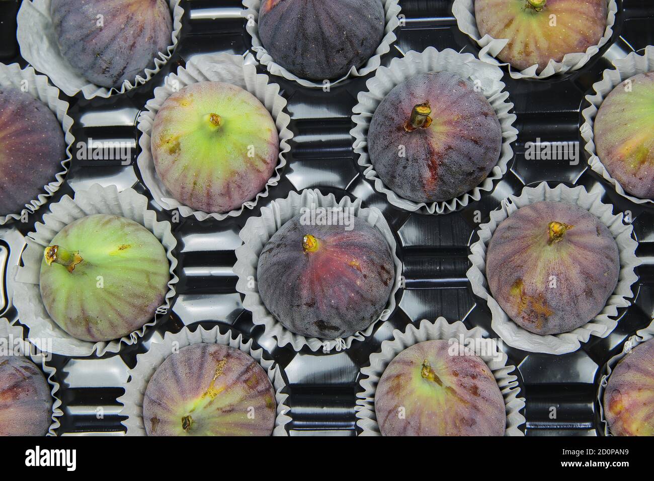 Hochwinkelansicht auf isolierten frischen reifen Feigen in Papier Cupcakes Tassen auf schwarzem Kunststofftablett Stockfoto