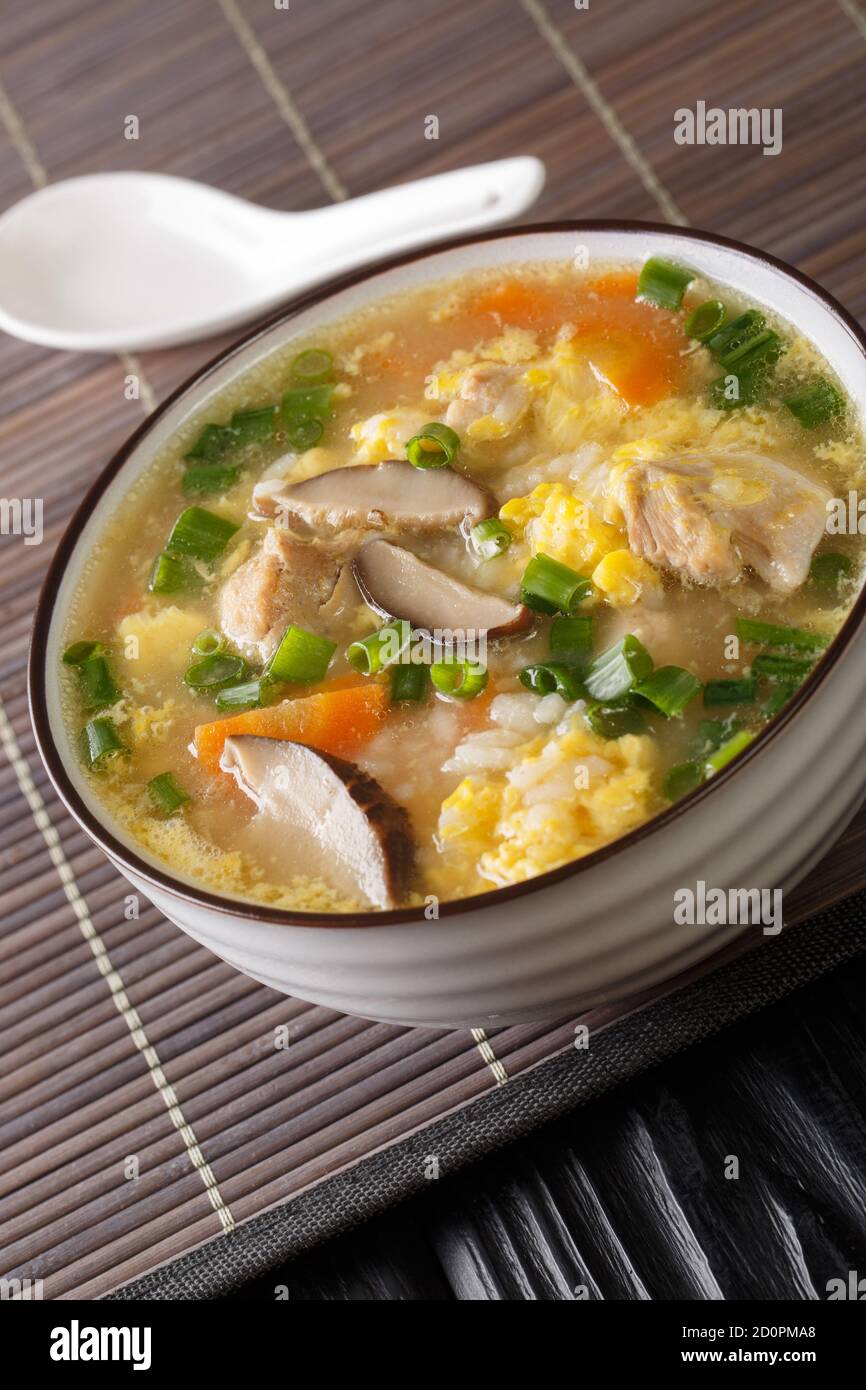 Zosui ist eine beruhigende japanische Reissuppe, die in einer herzhaften Dashi-Brühe mit Gemüse, Eiern, Pilzen und Hühnchen aus nächster Nähe in einer Schüssel auf dem Tisch zubereitet wird. Stockfoto