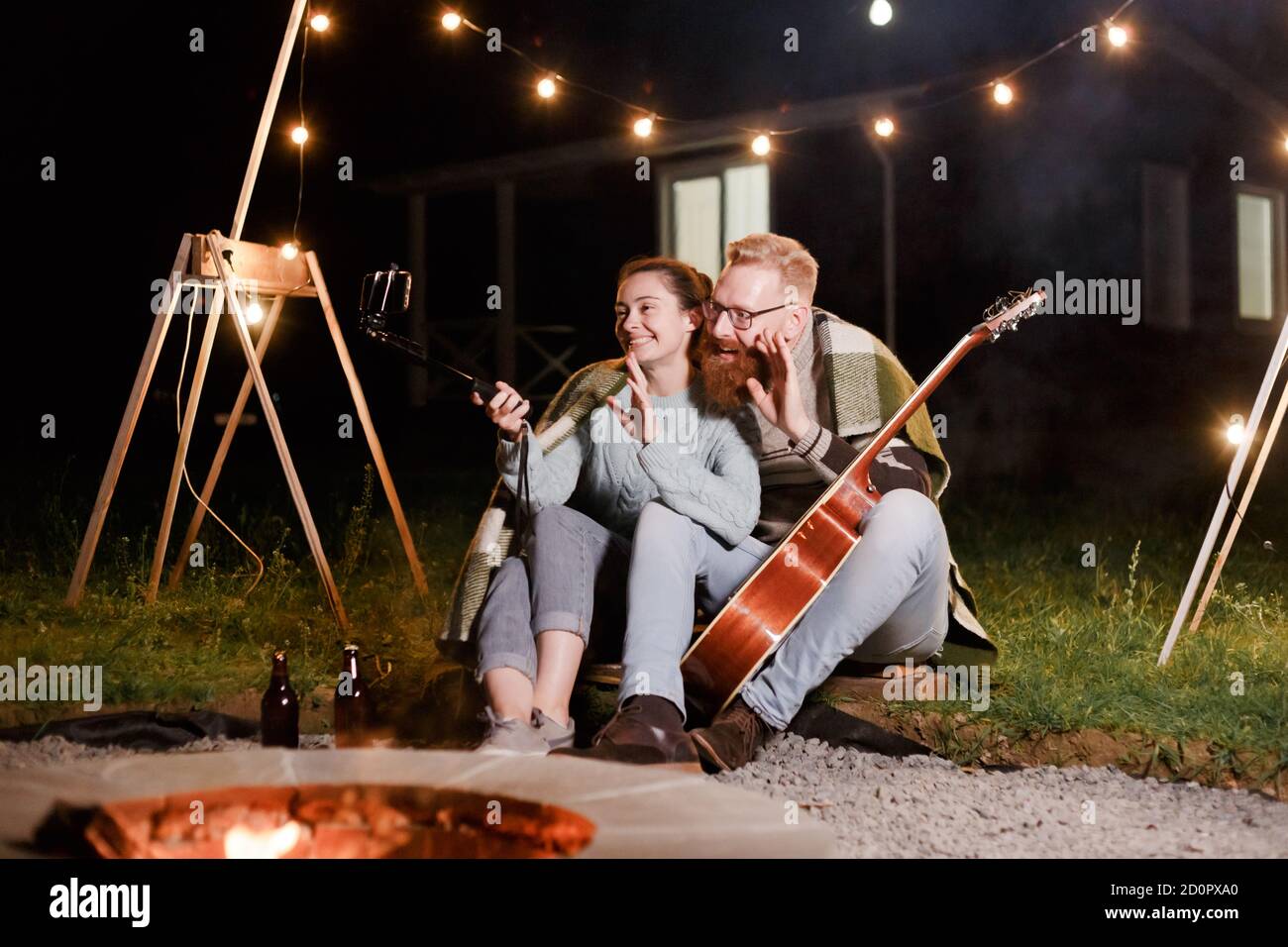 Glückliches kaukasisches Paar, Brünette Frau und bärtiger Mann mit Gitarre bei Picknick auf dem Land. Lustiges Paar macht Selfie, lächelt und hat Spaß zusammen Stockfoto
