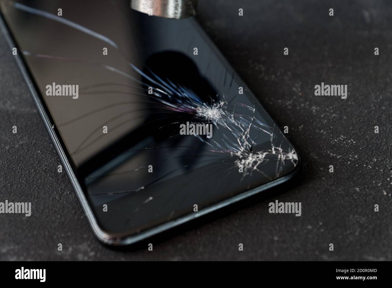 Smartphone mit kaputtem Glasschirm und Hammer auf dunklem Hintergrund. Stockfoto