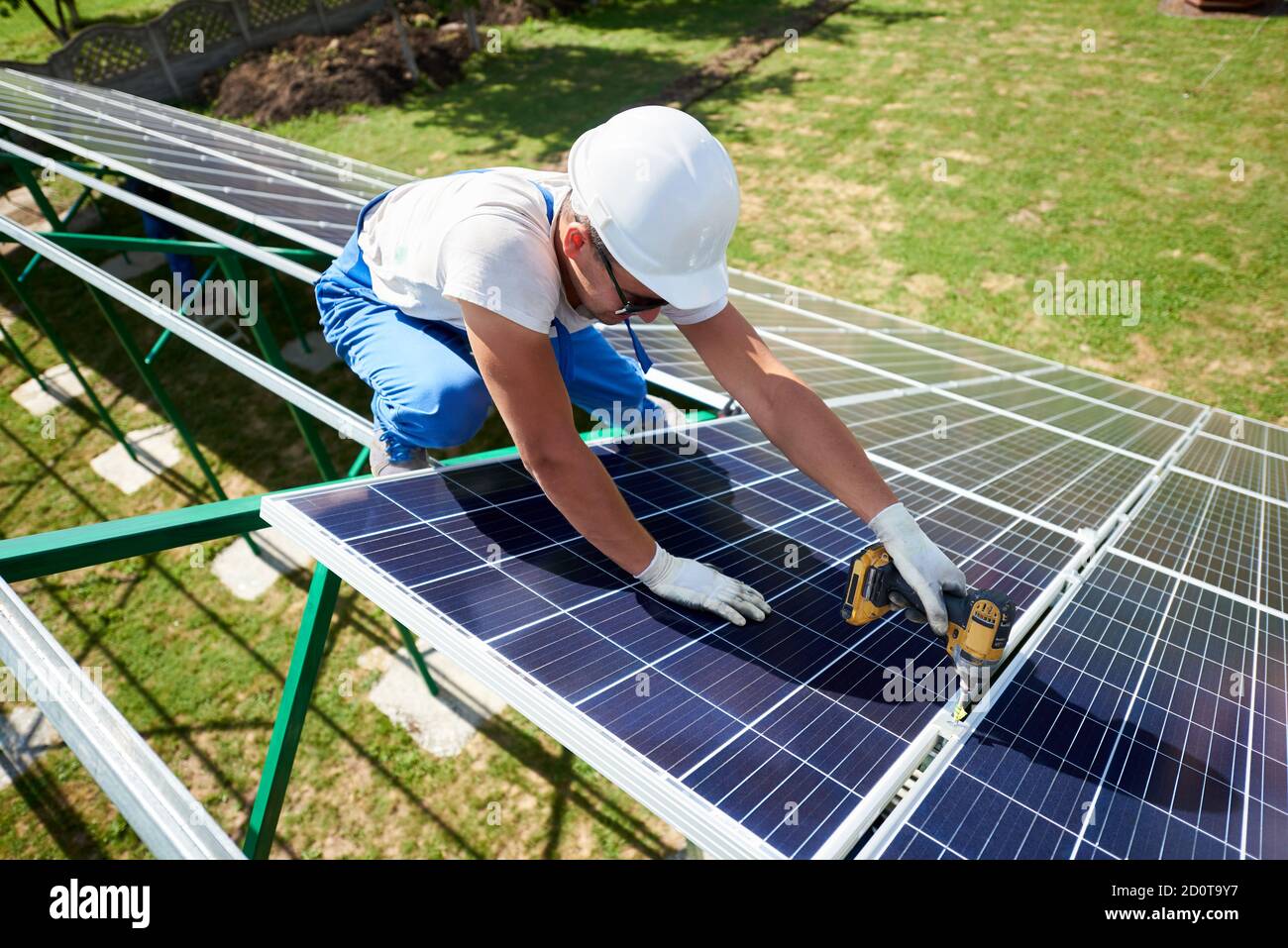 Facharbeiter, die Solarpaneele auf der grünen Metallkonstruktion installieren, verwenden verschiedene Geräte und tragen Helm. Innovative Lösung für die Energielösung. Nutzung erneuerbarer Ressourcen. Grüne Energie. Stockfoto