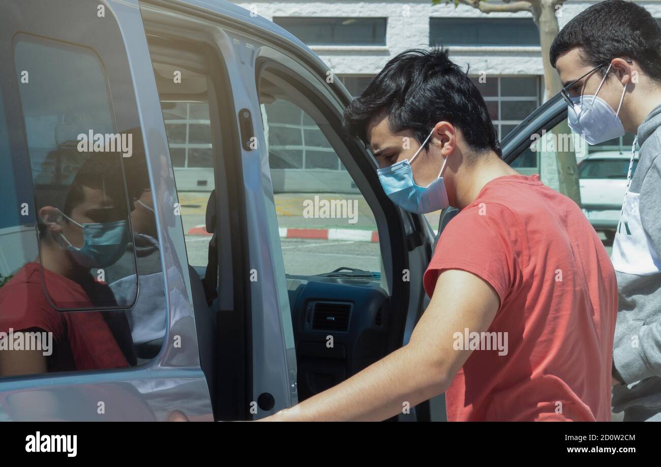 Zwei junge Männer, die mit dem Fahrzeug in ein Fahrzeug steigen 19 Virenschutzmasken Stockfoto