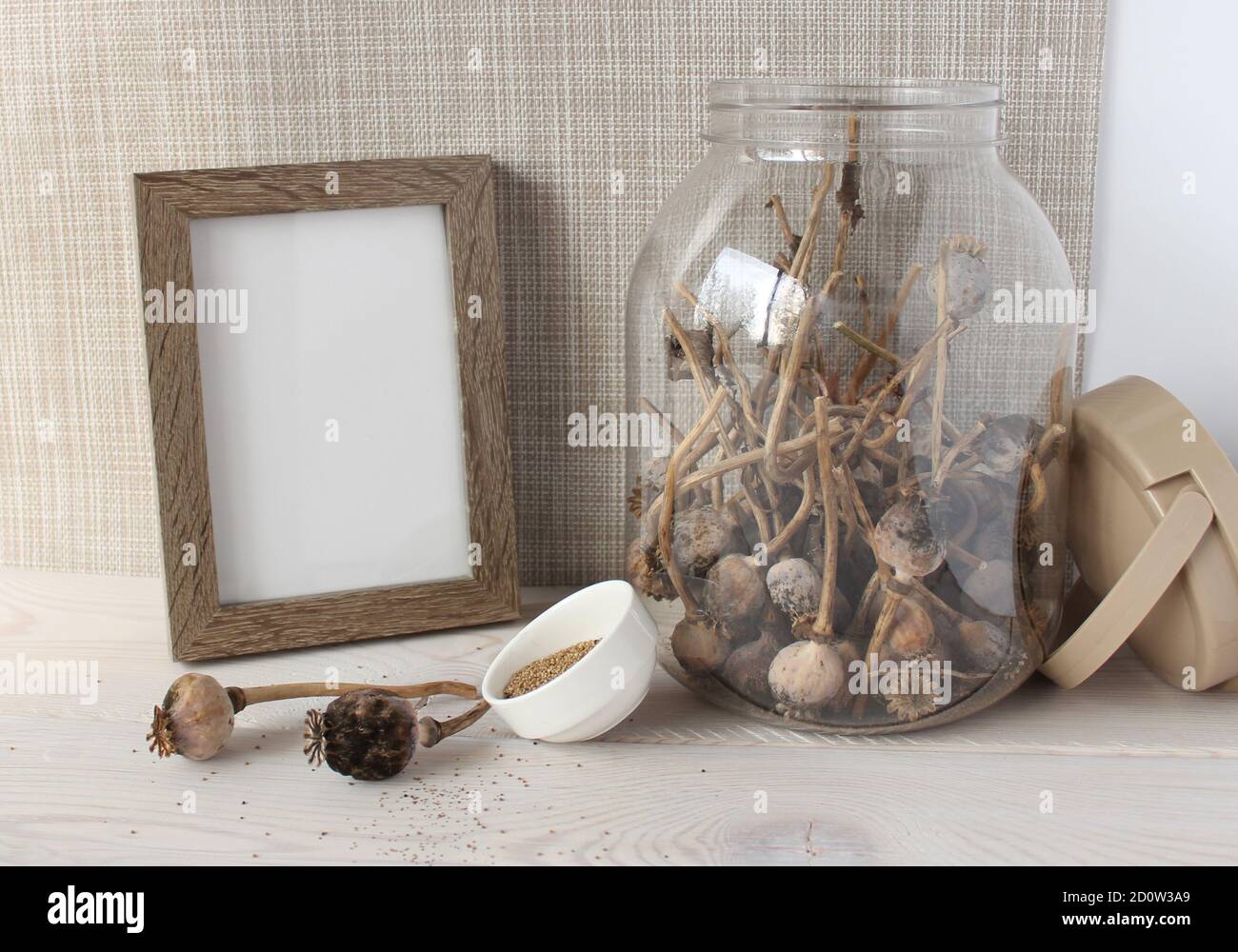Glas mit trockenen Mohnköpfen, Mohn Samen in einem weißen Cup, Holz Fotorahmen. Stockfoto