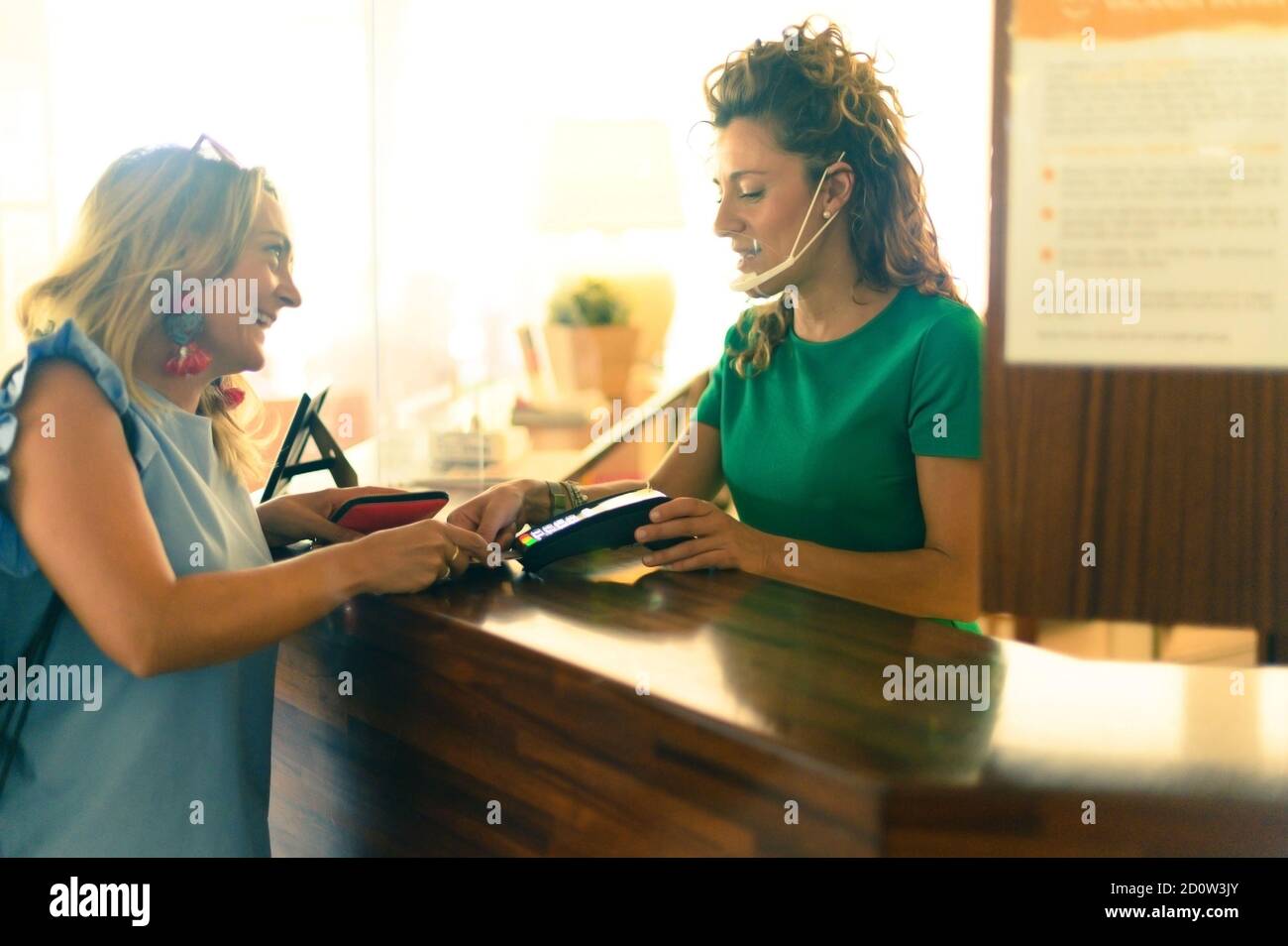 Kunde zahlt mit kontaktloser Kreditkarte - Barkeeper mit einem Kreditkartenlesegerät an der Theke mit weiblicher Holding Kreditkarte - Fokus auf Stockfoto