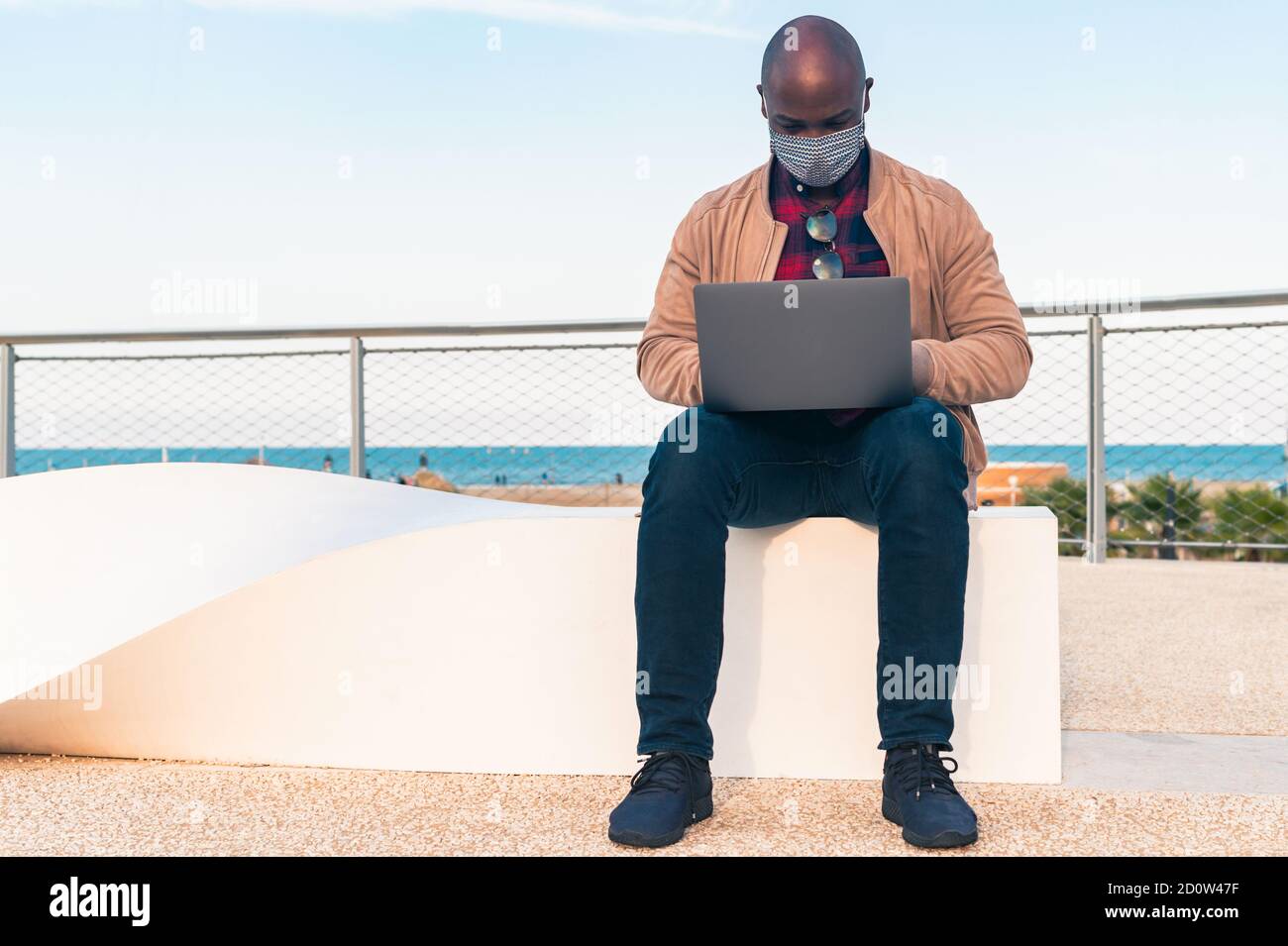 Schwarzer Mann mit der Gesichtsmaske, Arbeit auf Laptop sitzen auf einer Bank im Park - afroamerikanischen Geschäftsmann Blick auf Laptop-Bildschirm Gespräch mit Fr. Stockfoto