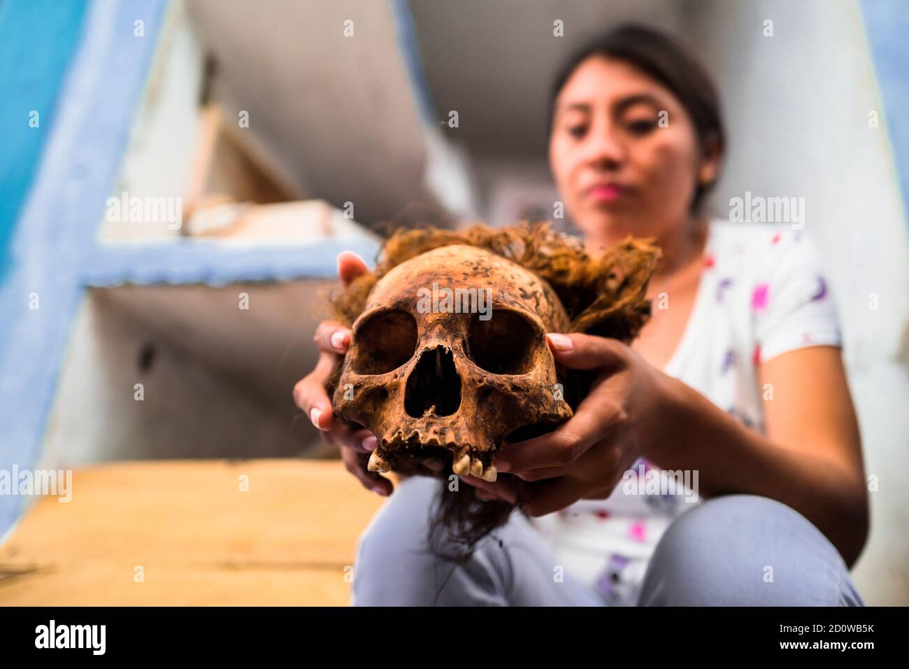 Eine junge Maya-Frau hält einen ausgetrockneten Schädel ihrer verstorbenen Großmutter während des Knochenreinigungsrituals auf dem Friedhof in Pomuch, Mexiko. Stockfoto