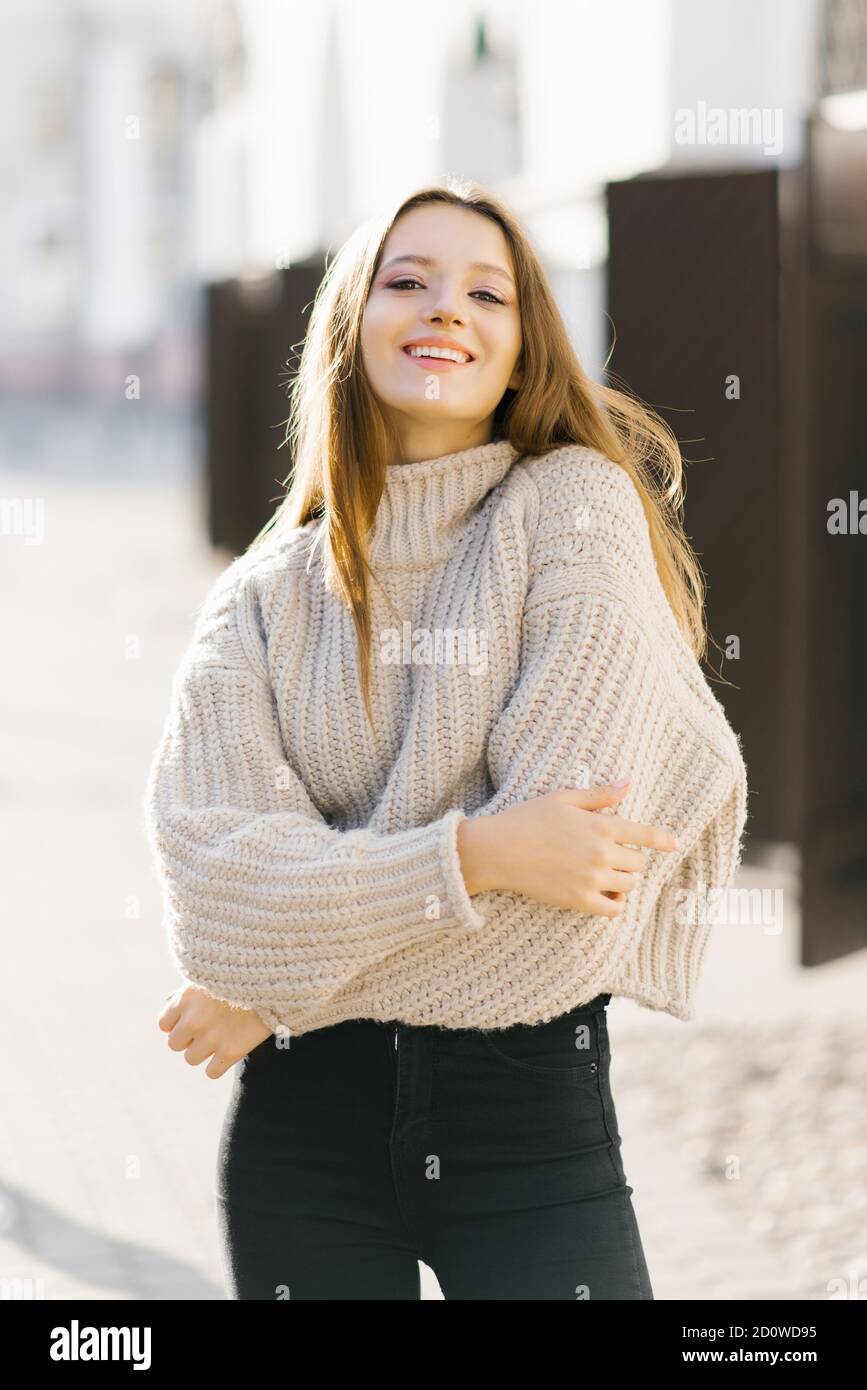 Eine junge Frau in einem beigefarbenen Strickpullover geht herum Die Stadt und lächelt wunderschön Stockfoto