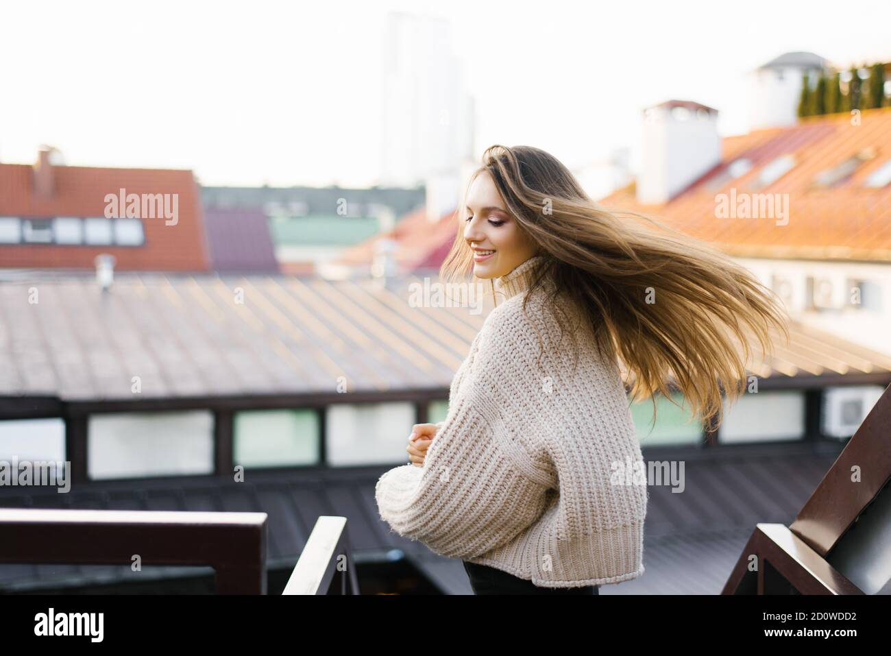 Eine schöne junge Brünette lächelt breit, ihre Haare entwickeln sich im Wind, während sie sich dreht. Porträt einer hübschen weiblichen Modell in einem modischen Stockfoto