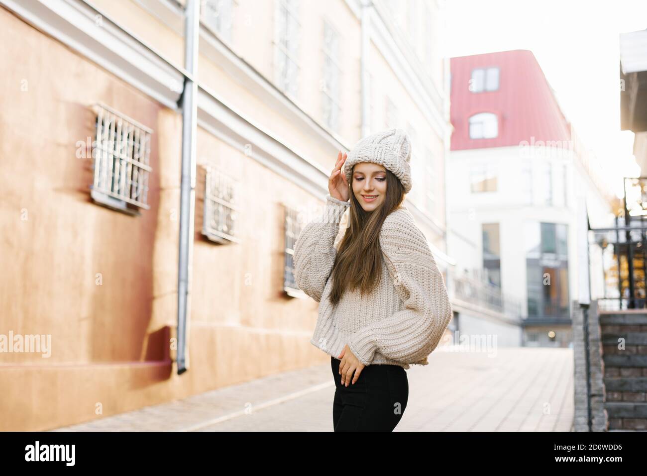 Charmante junge braunhaarige Frau auf einem Spaziergang. Eine schöne und glückliche Frau in einem stilvollen Bild in einem gestrickten warmen Hut. Spaziergang durch die Stadt, Lifestyle Stockfoto