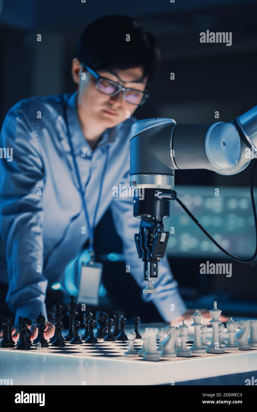 Vertikale Aufnahme eines professionellen japanischen Entwicklungsingenieurs, der eine testing Künstliche Intelligenz Schnittstelle durch das Spielen von Schach mit einem futuristischen Roboter Stockfoto