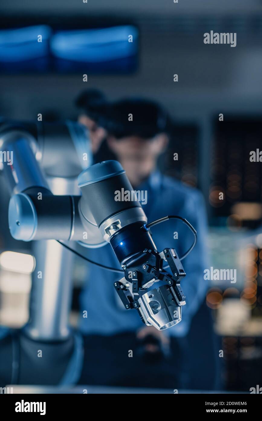 Vertikale Nahaufnahme eines futuristischen Roboterarms, gesteuert von Professional Development Engineer mit Virtual Reality Headset und Joysticks in A Stockfoto