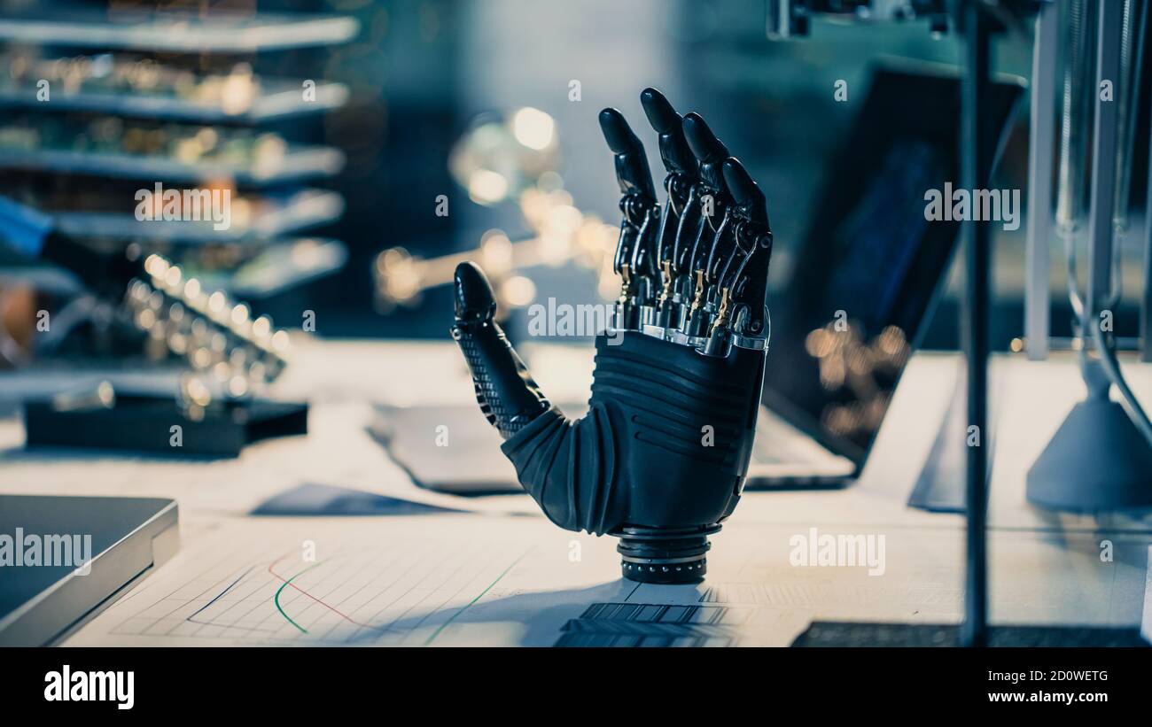 Nahaufnahme eines futuristischen prothetischen Roboterarms steht auf einem Schreibtisch in einem High-Tech-Forschungslabor mit moderner Computerausstattung. Stockfoto