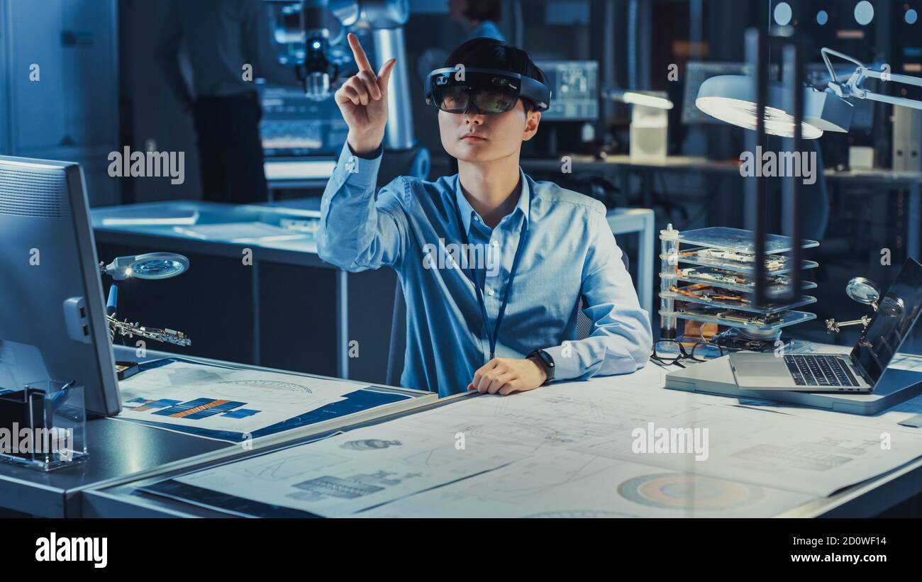 Professioneller japanischer Entwicklungsingenieur arbeitet in einem AR-Headset und macht Gesten, die virtuelle Grafikstücke in der High-Tech-Forschung berühren Stockfoto