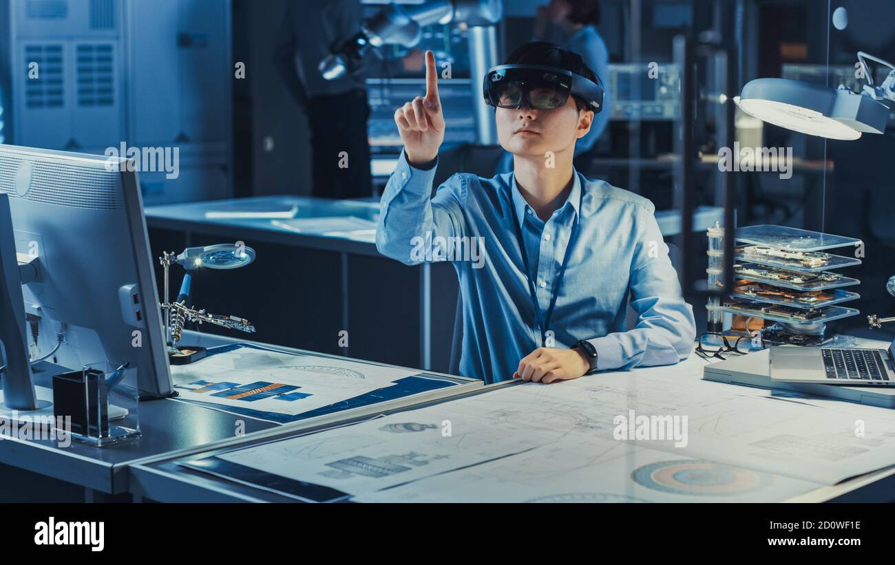 Der professionelle japanische Entwicklungsingenieur arbeitet in einem AR-Headset und macht Gesten, um virtuelle Grafikstücke in der High-Tech-Technologie zu bewegen Stockfoto