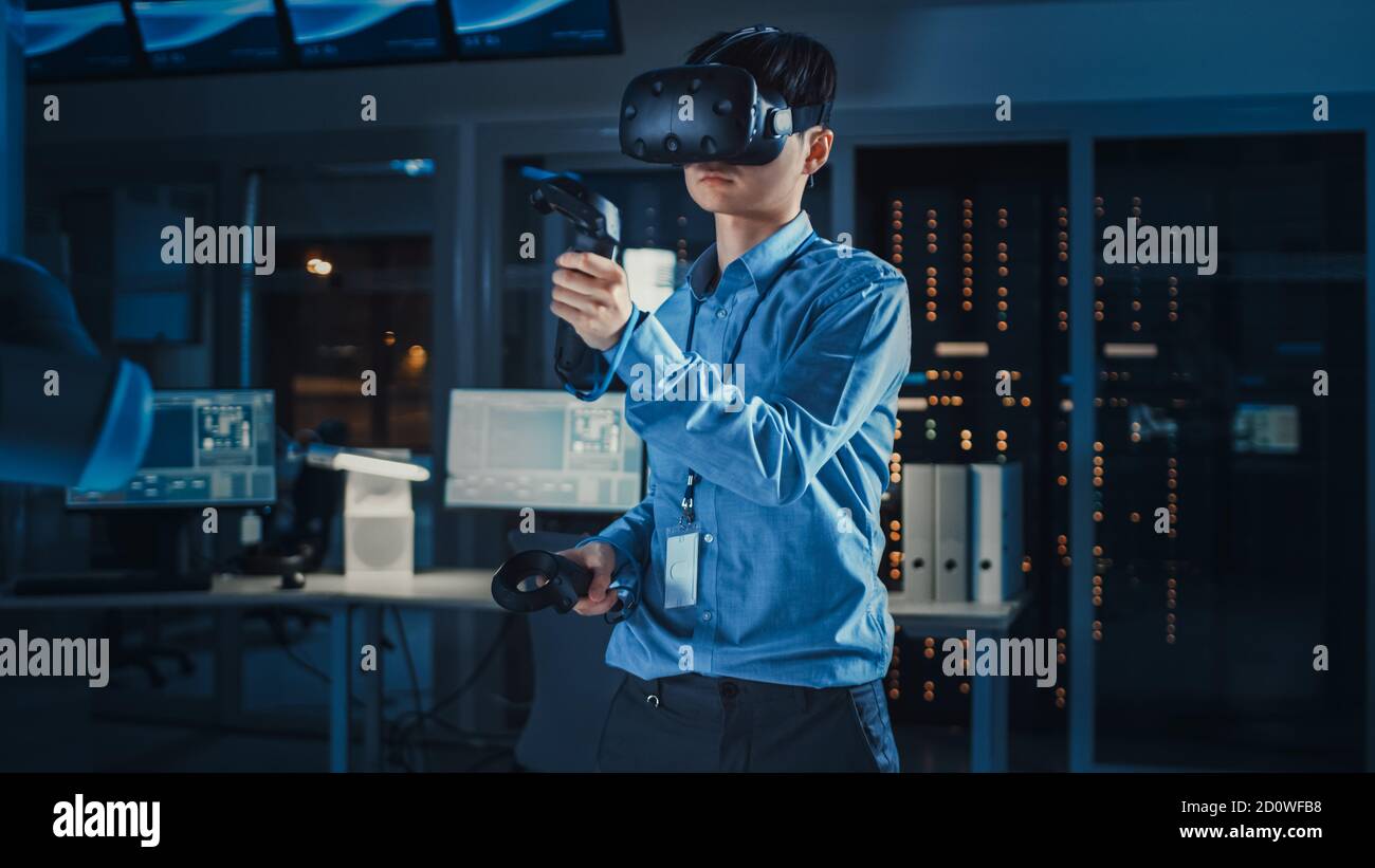 Professioneller japanischer Entwicklungsingenieur in blauem Hemd verwendet Augmented Reality-Headset und Joysticks in einem High-Tech-Forschungslabor Mit Stockfoto